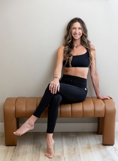 Smiling woman in black activewear sitting on a brown bench.