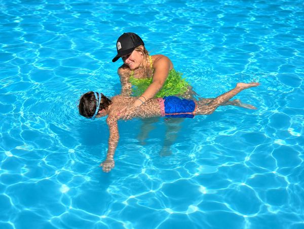 Woman teaching a child to swim in a bright blue pool.