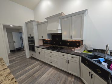 Modern kitchen with white cabinets, dark countertops, and wood-look flooring.