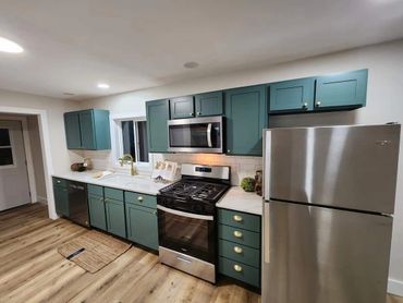 Modern kitchen with green cabinets and stainless steel appliances.