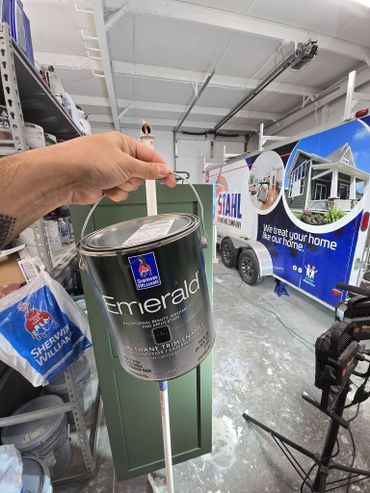 Hand holding Sherwin-Williams Emerald paint can in a painting workshop.