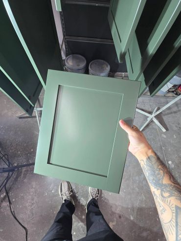 Person holding a freshly painted green cabinet door in a workshop.