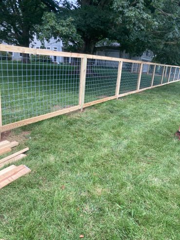 Newly installed wooden fence with wire mesh panels on a grassy lawn.