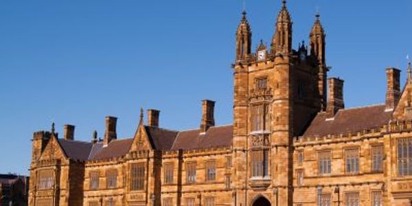 Historic sandstone university building under clear blue sky.
