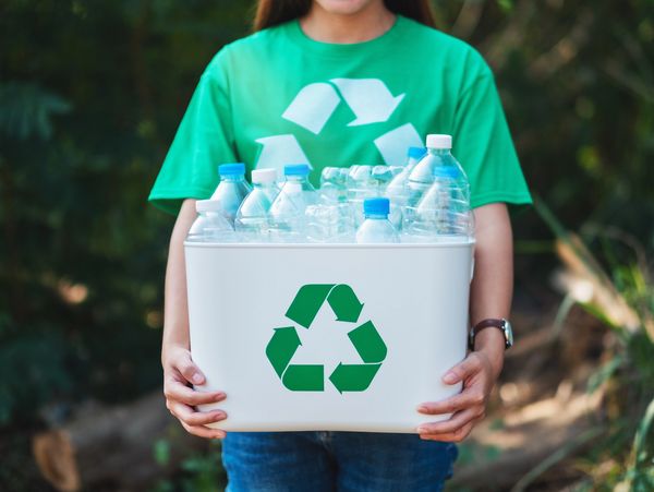 A person holding a bin with plastic bottles