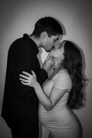 Couple sharing a tender kiss, woman visibly pregnant.