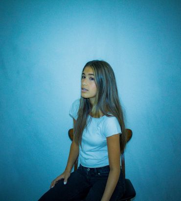 Young woman with braces sitting on a chair against blue wall.