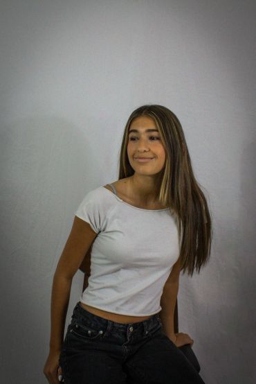 Young woman with long hair smiling, sitting on a chair.