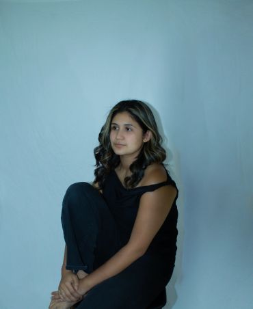 Young woman with wavy hair sitting and looking thoughtful.