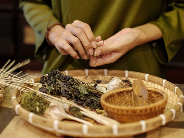 A person's hands sorting dried herbs and other natural ingredients on a woven tray