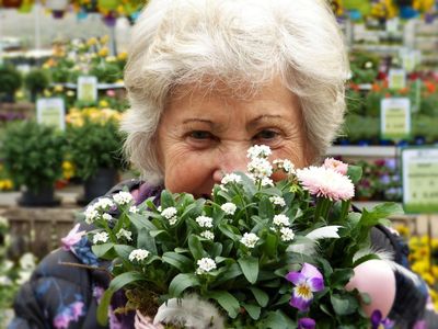 Smiling woman holds up a bunch of flowers as she shops for plants to add to her home garden.