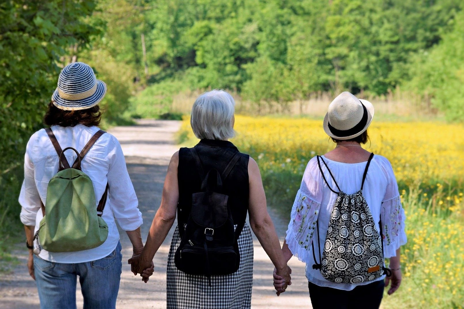 Three active women walking hand in hand through a green meadow on a sunny day.
