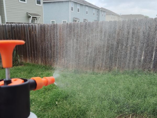A garden sprayer misting water over a green lawn near a wooden fence.