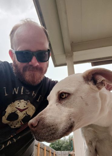 Man wearing sunglasses with a large white dog outdoors.