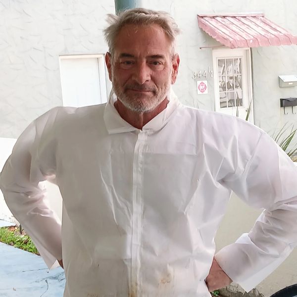 Man wearing a protective white suit with hands on hips.