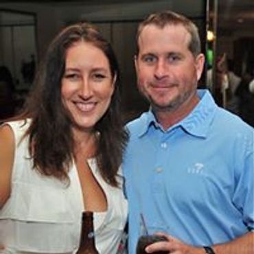 A smiling couple posing together at a social event, each holding a drink.