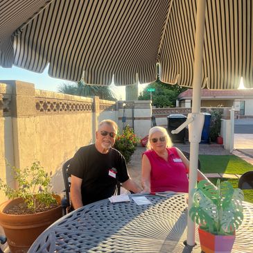 Two elderly people sitting outdoors under a striped umbrella.