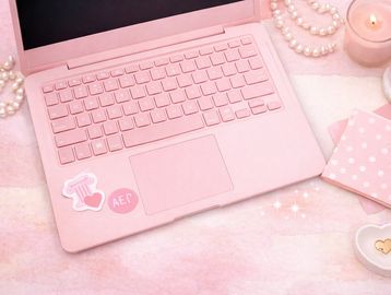 Pink-themed workspace with a laptop, pearls, candle, and heart-shaped dish.
