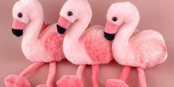 Three pink plush flamingo toys sitting side by side against a pink backdrop.