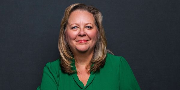 Smiling woman in a green blouse against a dark background.