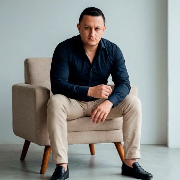 Man in black shirt and beige pants sitting on a beige armchair.