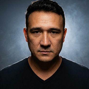 Serious man with dark hair and a black shirt against a smoky background.