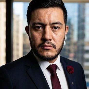 Confident man in suit with maroon tie and lapel flower.