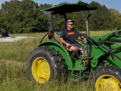 Man driving a green tractor in a grassy field on a sunny day.