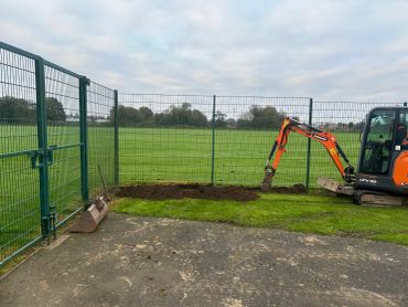 Excavator digging soil near green fence in open field.