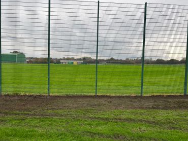 Green field behind a wire fence on a cloudy day.