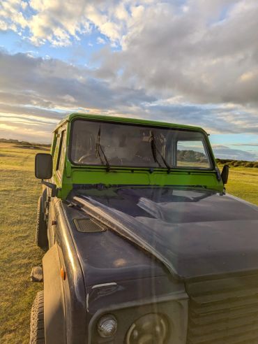 Close-up of an old black and green off-road vehicle in a grassy field.