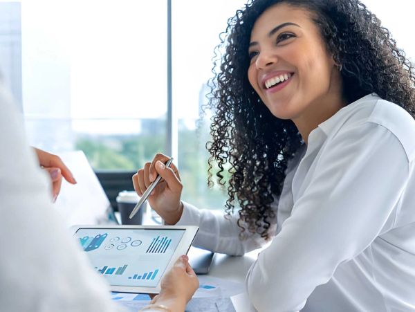 A woman smiling while discussing data on a tablet.
