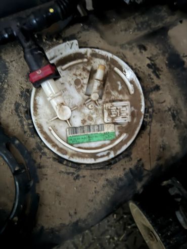 Dirty round plastic component with attached hoses on a dusty surface.