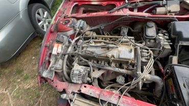 Dusty car engine in a red vehicle with visible wiring and components.