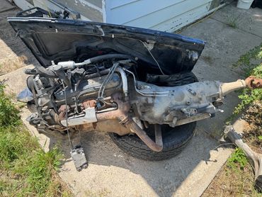 An old car engine with transmission placed on a tire outdoors.