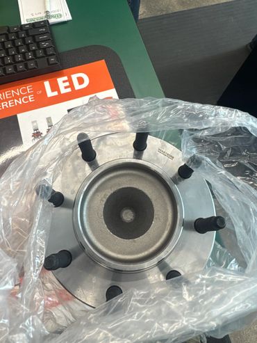 A metal automotive part with studs, partially wrapped in plastic.