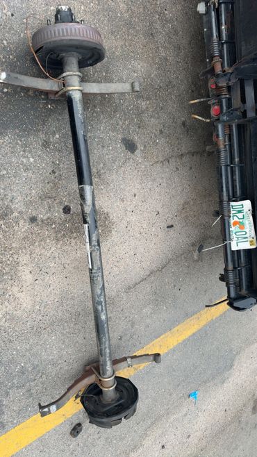 Rusty rear axle assembly with leaf springs on pavement near a vehicle with Florida license plate.