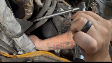 A tattooed arm working on machinery with a wrench held in hand.