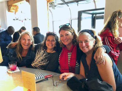 Four women smiling and sitting together at a table in a cozy cafe.