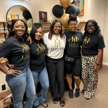 Five women smiling together wearing matching IHHD event shirts indoors.