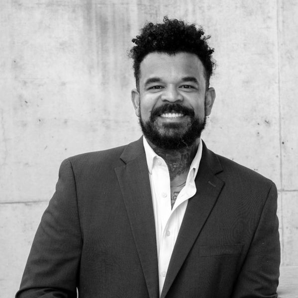 Man in suit smiling against a plain wall.