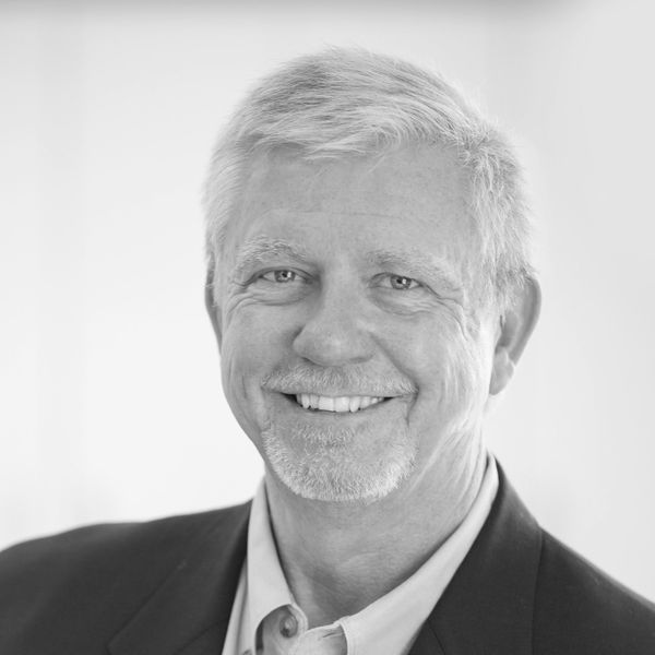 Smiling elderly man with white hair in a suit jacket.
