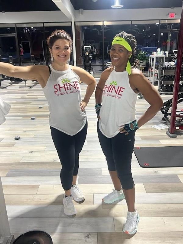 Two women in a gym wearing matching workout shirts and smiling.