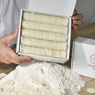 A box of white communion wafers held above a pile of flour and wafers on a table.