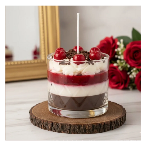 Layered dessert candle with cherries and chocolate on a wooden coaster.