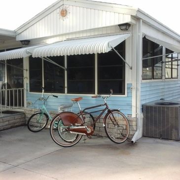Two bicycles parked beside a blue and white house with an air conditioning unit.