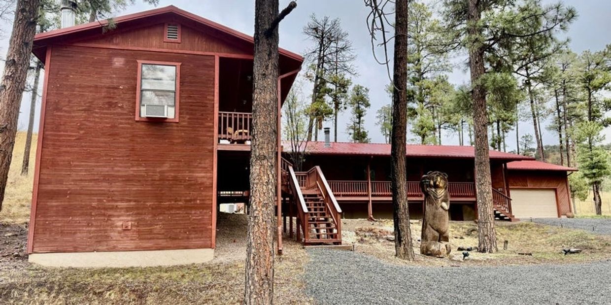 Rustic wooden cabin surrounded by tall pine trees with a carved bear statue.