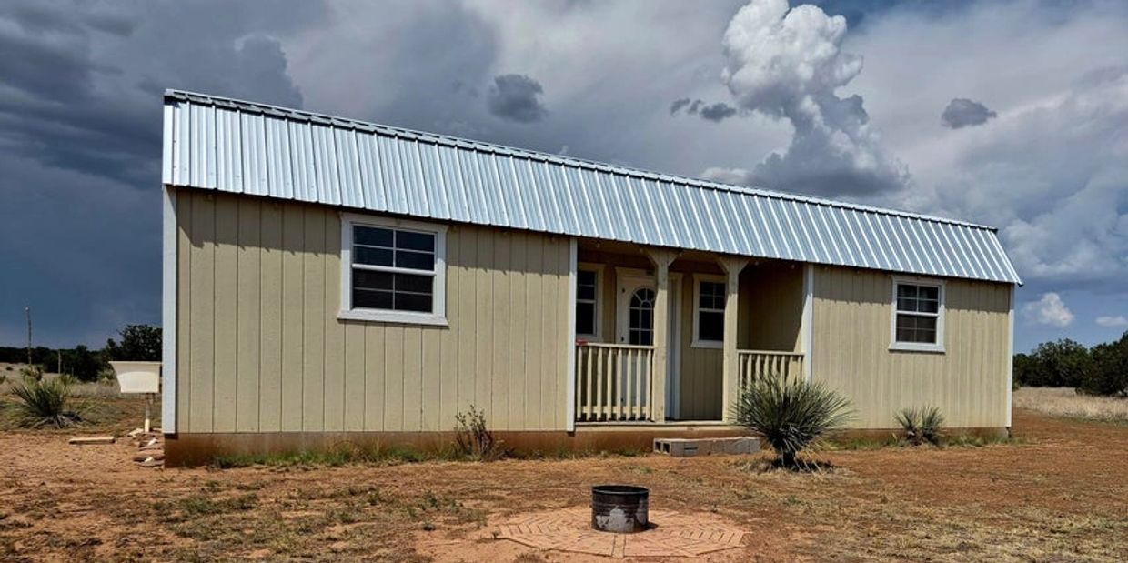 Small beige house with metal roof under moody sky.