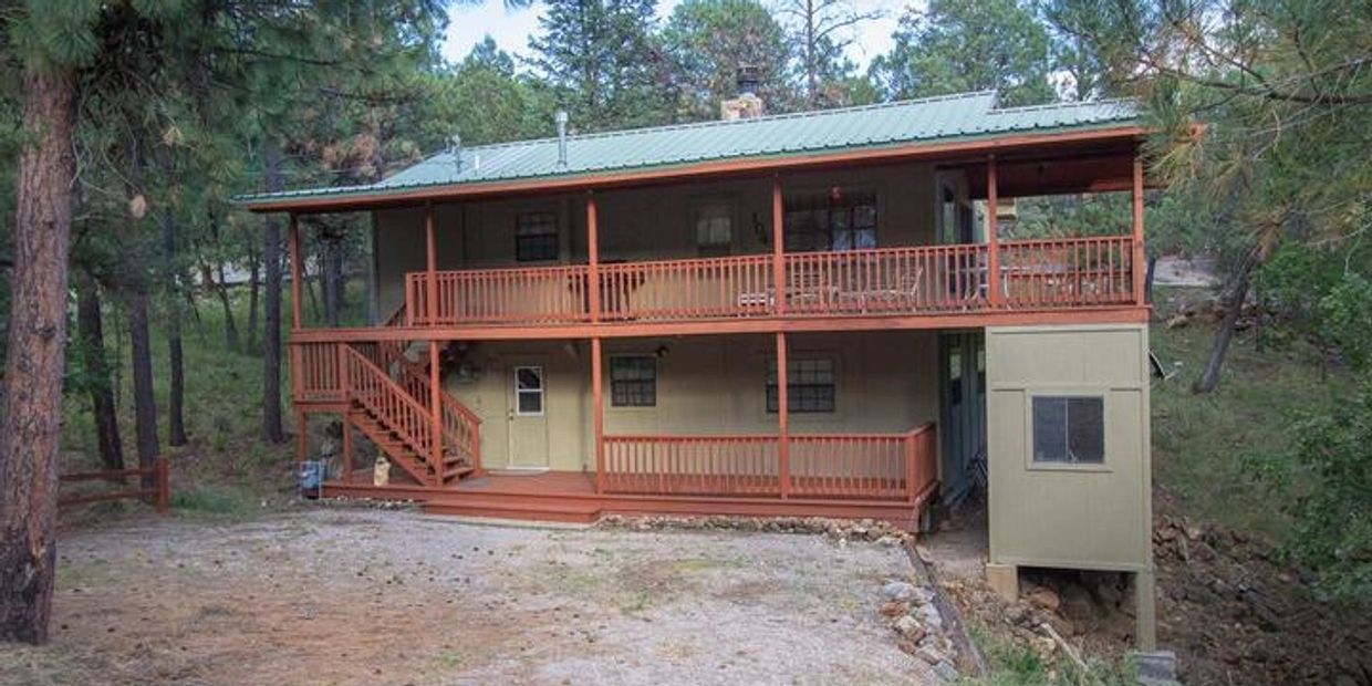 Two-story cabin with wooden porch in forest.