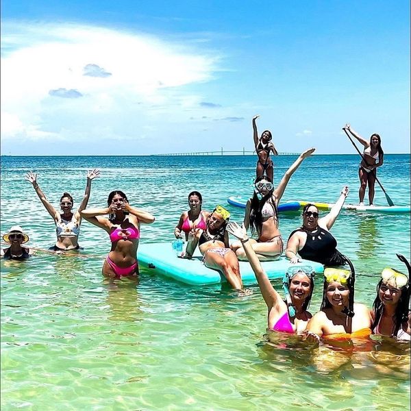 Group of women enjoying a sunny day at the beach, some on paddleboards and others in the water.